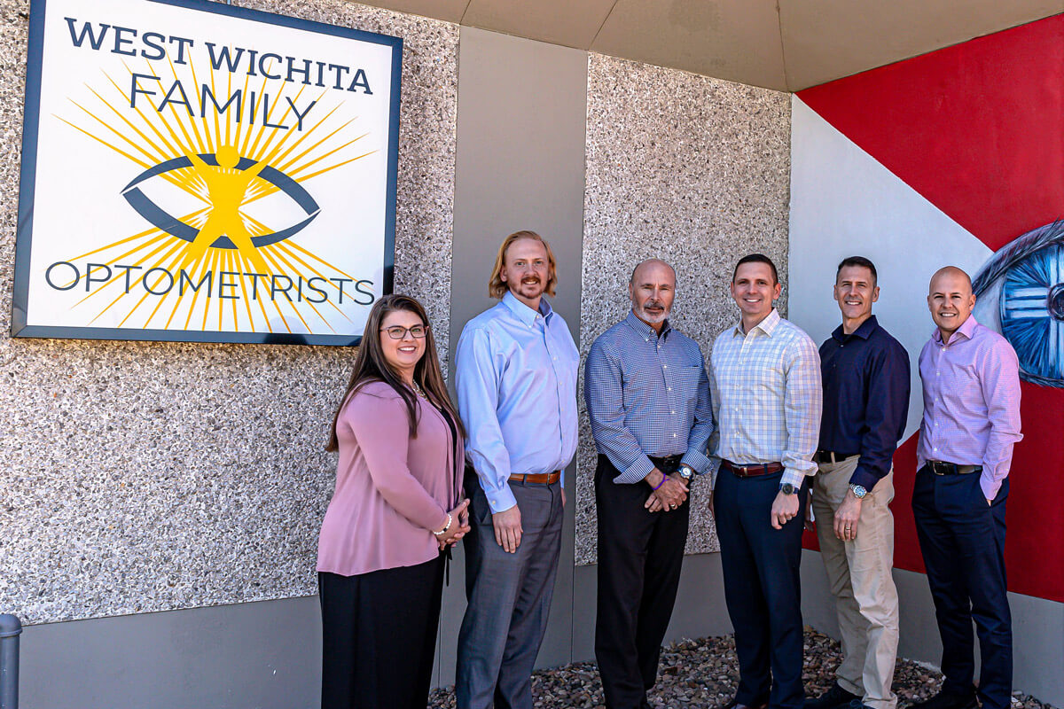 West Wichita Family Optometrists staff standing in front of the building, which has a Wichita Flag painted on the wall.